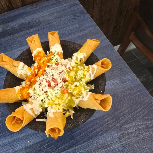 Crispy taquitos arranged in a circle, topped with red and green salsa, cheese, and crema.