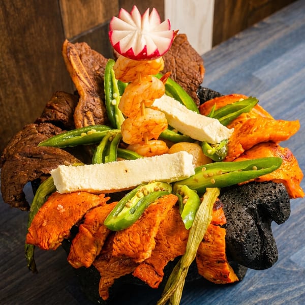 Molcajete dish with grilled meats, shrimp, cheese, and peppers, garnished with a radish.