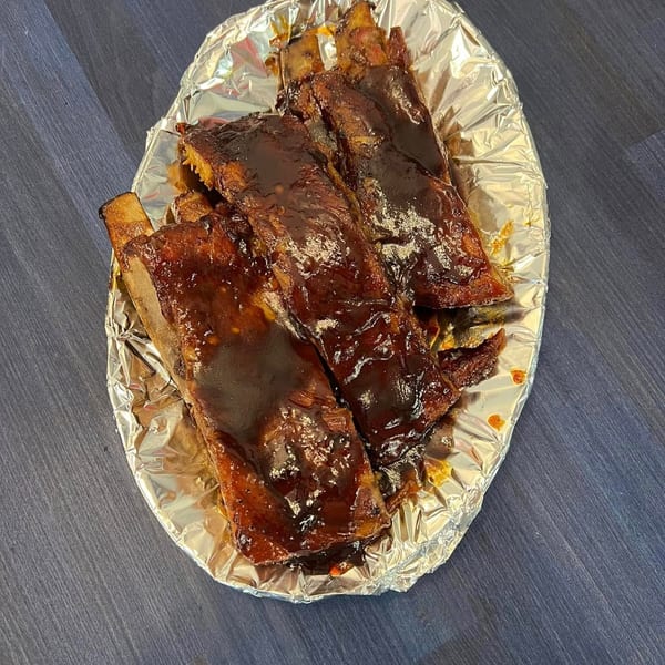 Glazed barbecue ribs and grilled meat arranged on a foil-lined tray over a dark wooden table.